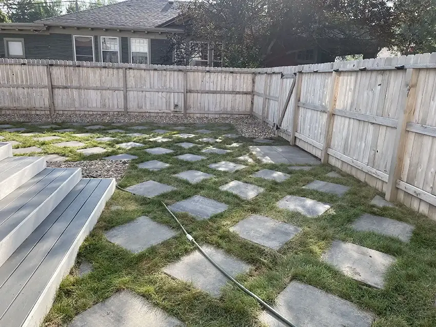 Backyard patio design with large square stepping stones set in grass, decorative rock edging, and composite deck stairs.